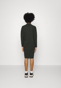 Robe tricotée vert foncé avec des manches longues, silhouette ajustée, ourlet côtelé et col montant, associée à des baskets sportives.