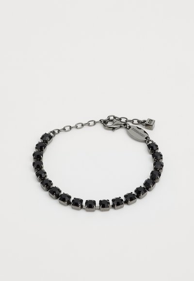 Bracelet en cristal noir avec un design en chaîne, des sertissages à griffes, un fermoir à clip et une petite étiquette en métal.