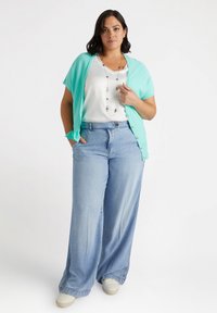 Lättviktig aqua cardigan över en vit blus, matchat med vida ljusblå jeans. Outfiten har minimala detaljer och en mjuk struktur.