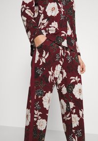 Burgundy floral pajama set featuring large white and black flowers, a relaxed fit, long sleeves, and pockets on the pants. Cotton fabric.
