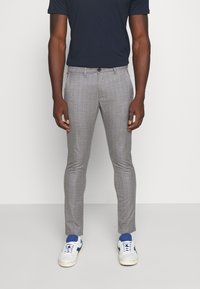 Šedé kostkované slim-fit kalhoty s knoflíkovým zapínáním, bočními kapsami a hladkým povrchem, spárované s bílými teniskami a námořnickým tričkem.