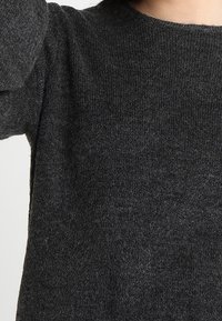 Maglione grigio scuro con scollatura tonda, polsi a costine e un morbido tessuto a maglia texturizzato. Inquadratura ravvicinata che mette a fuoco il tessuto e i dettagli delle maniche.