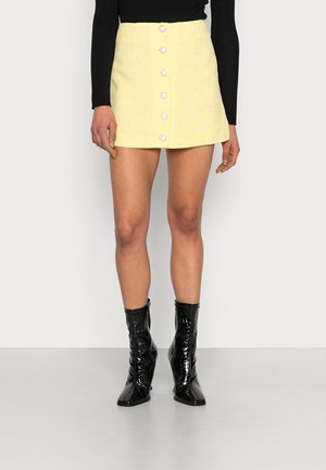 Geel mini-jurk met een gestructureerde stof, voorknopsluiting en een gladde afwerking. In combinatie met glanzende zwarte enkellaarsjes.