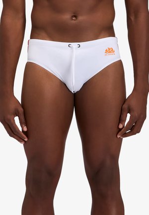 Torace e gambe maschili che indossano slip da bagno bianchi con un logo arancione Sundek sull'anca destra su sfondo bianco.