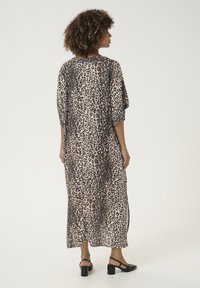 Maxi šaty s leopardím vzorom, vo voľnom strihu, s krátkymi rukávmi a jemnou, ľahkou tkaninou. Čierne topánky na blokovom podpätku dopĺňajú celý outfit.