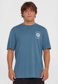 Camiseta de algodón azul con manga corta, cuello redondo y un gráfico en espiral impreso en blanco en el pecho. Textura suave, corte relajado.