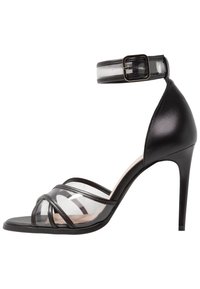 Svarta högklackade sandaler med genomskinliga remmar och snörning runt ankeln. Skon har en mjuk lädertextur med geometriska designelement.