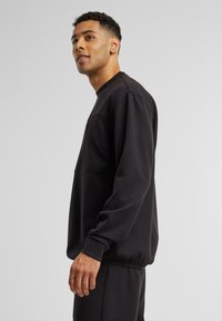 Czarny sweatshirt z żeberkowymi mankietami i dolnym wykończeniem, z kieszenią na piersi. Tkanina wydaje się miękka z luźnym krojem dla wygody.