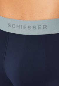 Marineblaue Boxershorts mit einem weichen elastischen Bund, der den Text "SCHIESSER" in hellgrau trägt. Glatte Stofftextur mit minimalen Nähten.