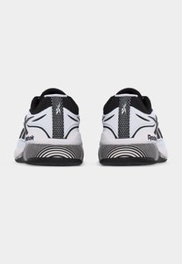 Ζευγάρι λευκών και μαύρων αθλητικών παπουτσιών Reebok, ορατά από πίσω, με σχέδια στη μέση σόλας και λογότυπα στις φτέρνες.