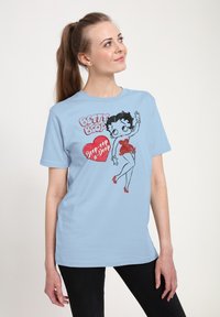Camiseta azul claro con un gráfico de Betty Boop vestida con un vestido rojo, con texto en negrita de colores negro y rojo. Material de algodón suave y casual.