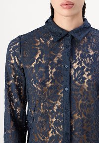 Marineblauw kanten shirt met bloemmotief, met knoopsluiting, kraag en doorzichtig textuur, voorzien van donkere knopen aan de voorkant.