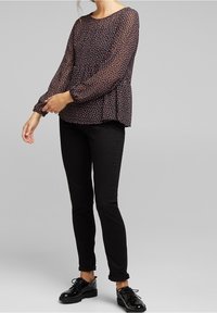Blusa nera a maniche lunghe, ampia, con motivo floreale. Abbinata a jeans skinny neri e scarpe nere lucide.