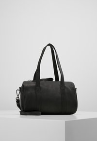 Czarna skórzana torba podróżna z dwoma krótkimi uchwytami i odpinanym paskiem, o gładkiej fakturze i cylindrycznym kształcie. Srebrne akcenty metalowe.