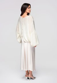 Pull en tricot blanc et duveteux avec des manches surdimensionnées et un détail de boutons au dos, associé à une jupe en satin rose clair et des talons à brides.