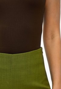 Haut marron sans manches associé à un pantalon vert taille haute. Le tissu semble lisse avec une légère texture et des lignes nettes et ajustées.