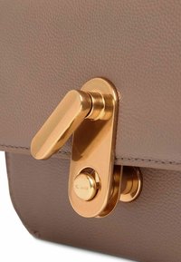 Cierre de bolso de cuero marrón texturizado con una hebilla metálica dorada y pulida. La hebilla tiene un pomo redondeado y una palanca plana para un cierre seguro.