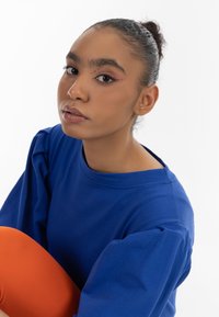 Királykék pulóver puffos ujjal, élénk narancssárga bordás leggingsszel párosítva; sima textúra, kerek nyakú, látható minták nélkül.