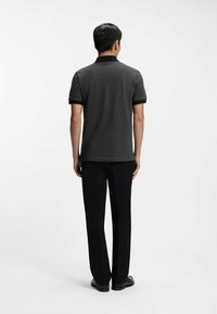 Tummanharmaa pikeepaita, jossa musta kaulus ja hihasomisteet, yhdistetty mustiin housuihin, nähtynä takaa.