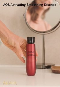 AHAVA AOS Activating Smoothing Essence in een slanke, glanzende rode fles met een zwarte dop. Bevat duidelijke tekst voor productidentificatie.