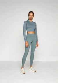 Világoskék sportos szett, amely egy rövidített hosszú ujjú felsőből és magasított derekú leggingsből áll. Puha, rugalmas anyag, sima textúrával.