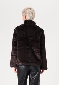 Kurtka z futerka ekologicznego w ciemnobrązowym kolorze, z wysokim kołnierzem i długimi rękawami. Gładka faktura z lekko połyskującym wykończeniem. Elegancki, nowoczesny design.