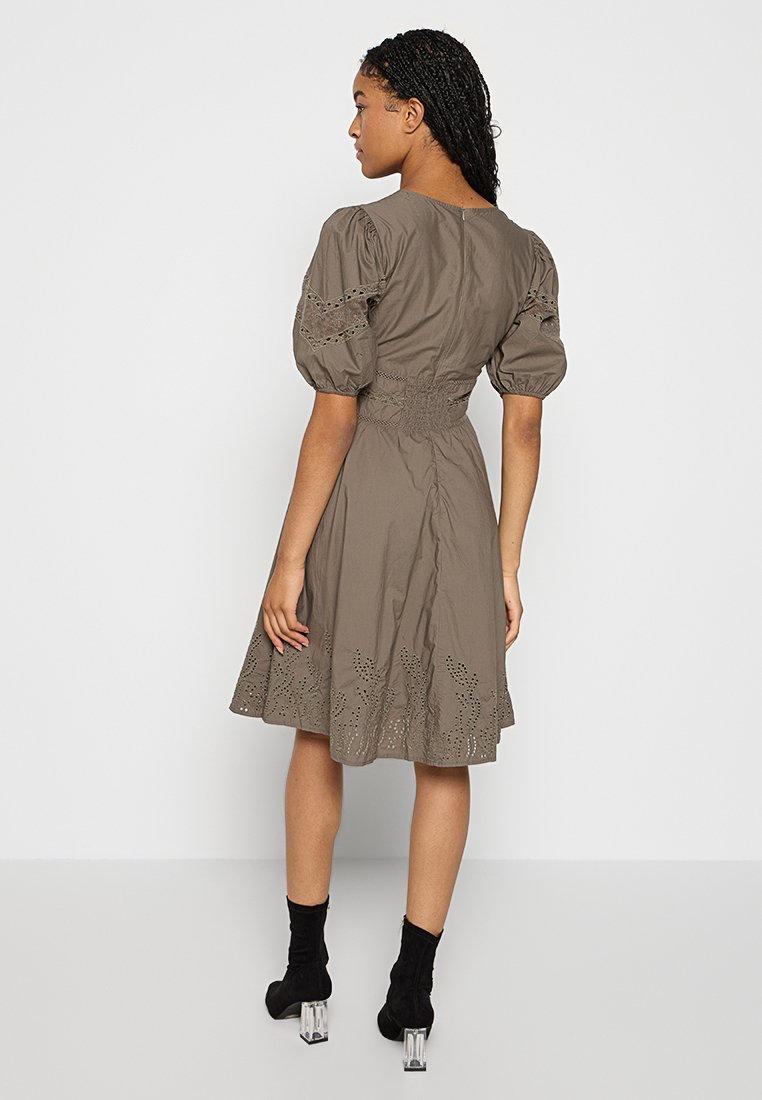 Braunes Kleid mit Puffärmeln, tailliertem Schnitt, bestickten Akzenten am Saum und einem ausgestellten Rock, getragen mit schwarzen Knöchelstiefeln.