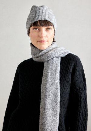 Gray knit beanie and a matching wide scarf made of soft, textured fabric. The scarf is draped around the neck over a black, textured sweater.
