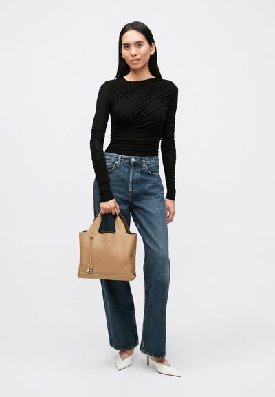 Torebka z brązowej skóry o usztywnionym kształcie, z dwoma uchwytami i zamkiem błyskawicznym. Połączona z czarną bluzką i niebieskimi prostymi jeansami.