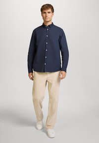 Camisa de botones azul marino de algodón, de manga larga, con cuello y botones en el frente, combinada con pantalones de pana beige y zapatillas blancas.