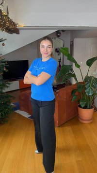 Blue short-sleeve t-shirt with logo, paired with black wide-leg trousers, and gray sneakers. Indoor setting with plants and furniture.