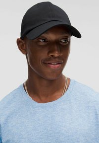 Black baseball cap with a rounded crown and curved visor, worn over a light blue textured crew neck t-shirt. Simple design, no logos.