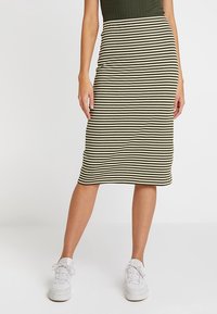 Pruhovaná žebrovaná midi sukně v olivově zelené a krémové barvě. Příjemný střih, měkká textura. Kombinováno s bílými teniskami, vyzařuje ležérní styl.