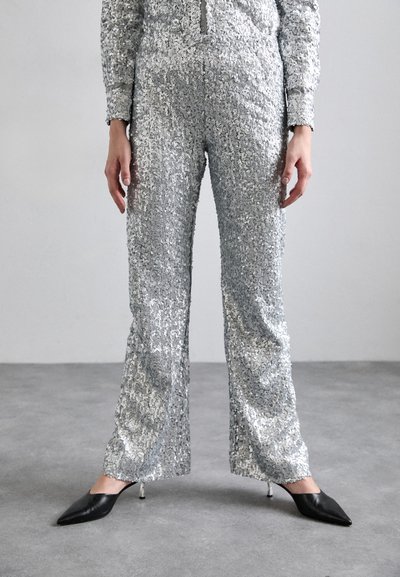 Sølv paljett jumpsuit med lange ermer, smal passform, kontrasterende grå detaljer og vide bukseben. Sammen med svarte stiletthæler.