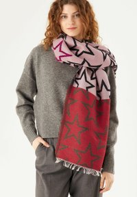 Écharpe tricotée avec une section supérieure rose ornée d'étoiles noires et une partie inférieure rouge avec de grands motifs d'étoiles noires ; bords à franges.