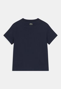 Mörkblå t-shirt i bomull med korta ärmar, ribbad rund halsringning och en liten grön krokodil-logotyp på baksidan. Slät textur.