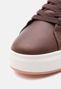 Καφέ δερμάτινο αθλητικό παπούτσι με  στρογγυλεμένη μύτη, διαθέτει παχύ λευκό πέλμα και υφή στην επιφάνεια, συμπληρωμένο με καφέ κορδόνια.