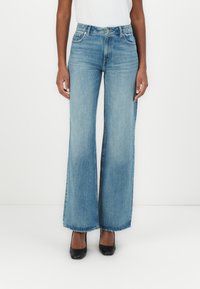 Pantalones vaqueros anchos de mezclilla en azul, con una cintura alta, cinco bolsillos y un lavado claro con un ligero desvanecimiento. El dobladillo es sin terminar.