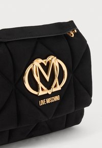 Black quilted handbag with a gold-tone logo and accent, featuring a smooth texture and structured shape. Zipper closure at the top.