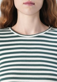 Zöld és fehér csíkozott, bordázott felső, kerek nyakkal. Az anyag texturális megjelenésű, változó szélességű csíkokkal.