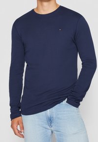 Navy long-sleeve t-shirt made of soft cotton with a crew neckline. Features a small logo accent on the chest and fitted sleeves.