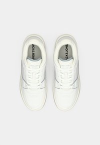 Bijele kožne tenisice s glatkom teksturom, sivoj akcentima, perforiranim detaljima i tradicionalnim sustavom vezanja. Logo je vidljiv unutar.