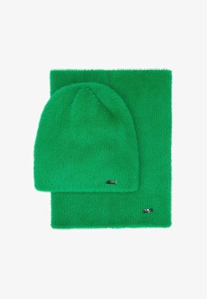 Zielony zestaw z polaru: czapka i szalik. Czapka jest miękka, z zaokrąglonym wierzchołkiem, a szalik ma podobną teksturę. Oba elementy mają małe metaliczne ozdoby.