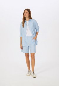 Light blue cotton button-up shirt with long sleeves, paired with matching tailored shorts. White graphic t-shirt underneath, silver sneakers.