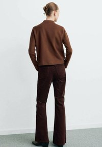 Pull en maille marron et pantalons en velours côtelé bordeaux foncé évasés. Les pantalons ont une poche arrière et une silhouette ajustée. Design simple et texturé.