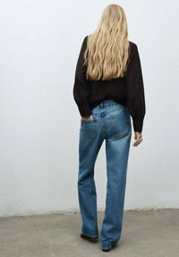 Blusa oscura de manga larga con mangas voluminosas combinada con Jeans de denim de tiro alto, de color azul claro, que cuentan con bolsillos traseros y un corte relajado.