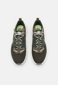 Mörkgrön och svart mesh-sneakers med vita och olivgröna accenter, som har en texturerad sula och flerfärgade prickar. Inkluderar snörning och sidostraps.