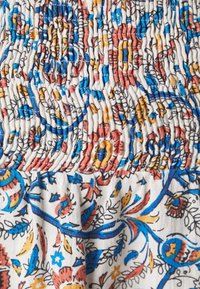 Tessuto con motivi floreali e di uccelli multicolori in blu, rosso, giallo e nero su uno sfondo bianco, con cuciture raccolte e con texture.