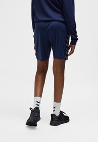 Navyblauwe korte broek met zwarte chevron-zijaccenten, gecombineerd met witte sokken met zwarte strepen en zwarte sportschoenen.