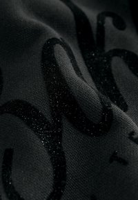 Primer plano de una tela negra con letras en relieve y texturizadas brillantes que crean un patrón decorativo brillante.